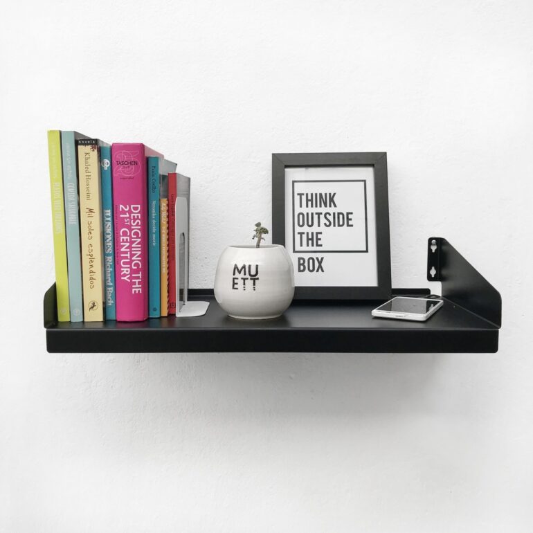 Estante FIT Muett negro con objetos decorativos, cuadro, con libros y celular con pasacables cargador en ambiente moderno
