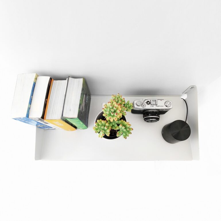Estante FIT Muett blanco con libros, maceta con planta pequeña, cámara de fotos y parlante con cable por pasacables ambiente moderno