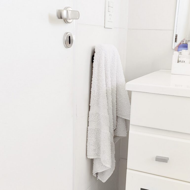 Gancho DOJO Mediano Muett instalado en pared de baño, diseño funcional moderno minimalista con toalla colgada