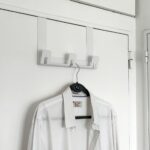 Perchero HANGA de acero plegado, color blanco instalado sobre puerta con camisa colgada, diseño moderno y minimalista Muett