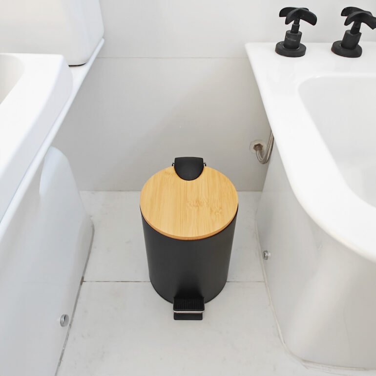 Tacho de basura NORD negro entre inodoro y bidet, con tapa de madera de estilo escandinavo.